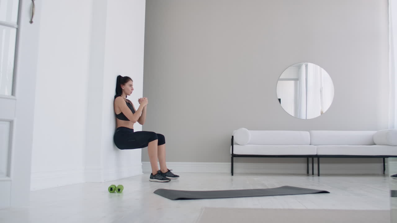 정적 위치에 있는 여성은 앉아있는 자세로 벽에 기대어 힘든 운동을 수행합니다.