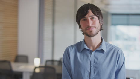 Portrait-Of-Smiling-Casually-Dressed-Businessman-Standing-In-Modern-Open-Plan-Office