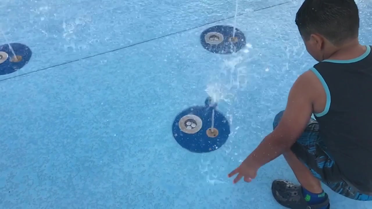 Criança brincando, tentando equilibrar uma bola em um jato de água ascendente