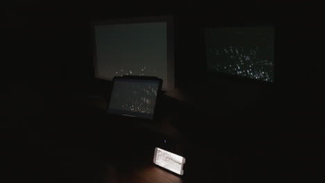 a side angle shot of four digital computer device screens flashing a strobing static noise pattern in a dark room