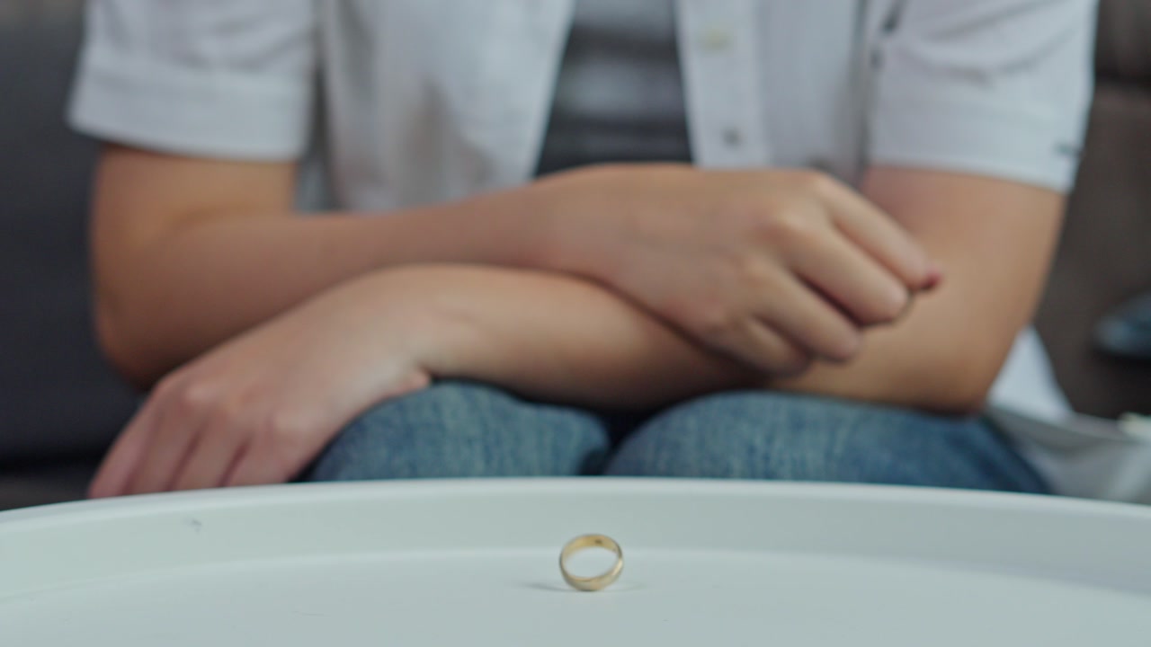 Close-up of wife hand spinning a wedding band on a table before clenching fist in frustration