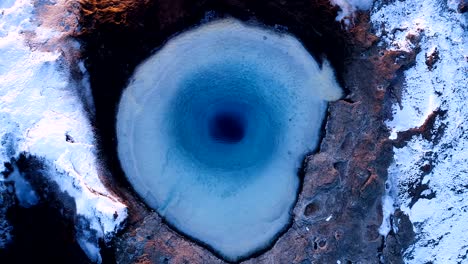 view of a drone which getting further and further of the center of a geuser in geysir, iceland . smoke is getting out of the geyser with people walking all around the geyser, under the red sunset.