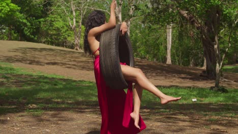 a young latina girl in a bright red dress swing on a tire in the wonders of a tropical caribbean park