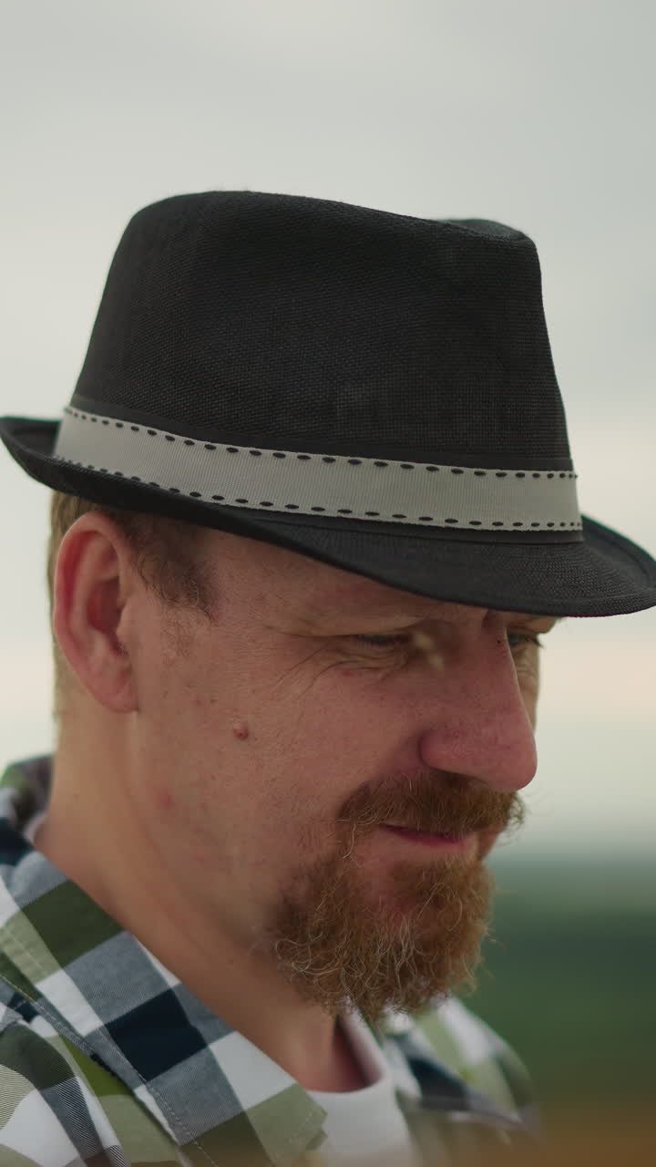 검은 모자와 초록색 체크 셔츠를 입은 남자의 클로즈업, 보이지 않는 작업에 깊이 초점을 맞추고, 배경에는 조용하고 초점 밖의 풍경이 있습니다.