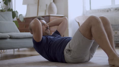 hombre barbudo guapo haciendo abdominales en el suelo en casa