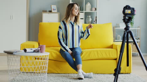 alegre bloguera hablando y mostrando los pulgares hacia arriba en la cámara mientras graba un video para sus seguidores sentados en un sofá amarillo en casa 1