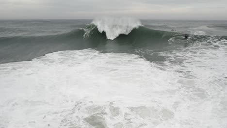 slow motion shot of big ocean wave breaking and splashing sea foam on overcast day, nazare