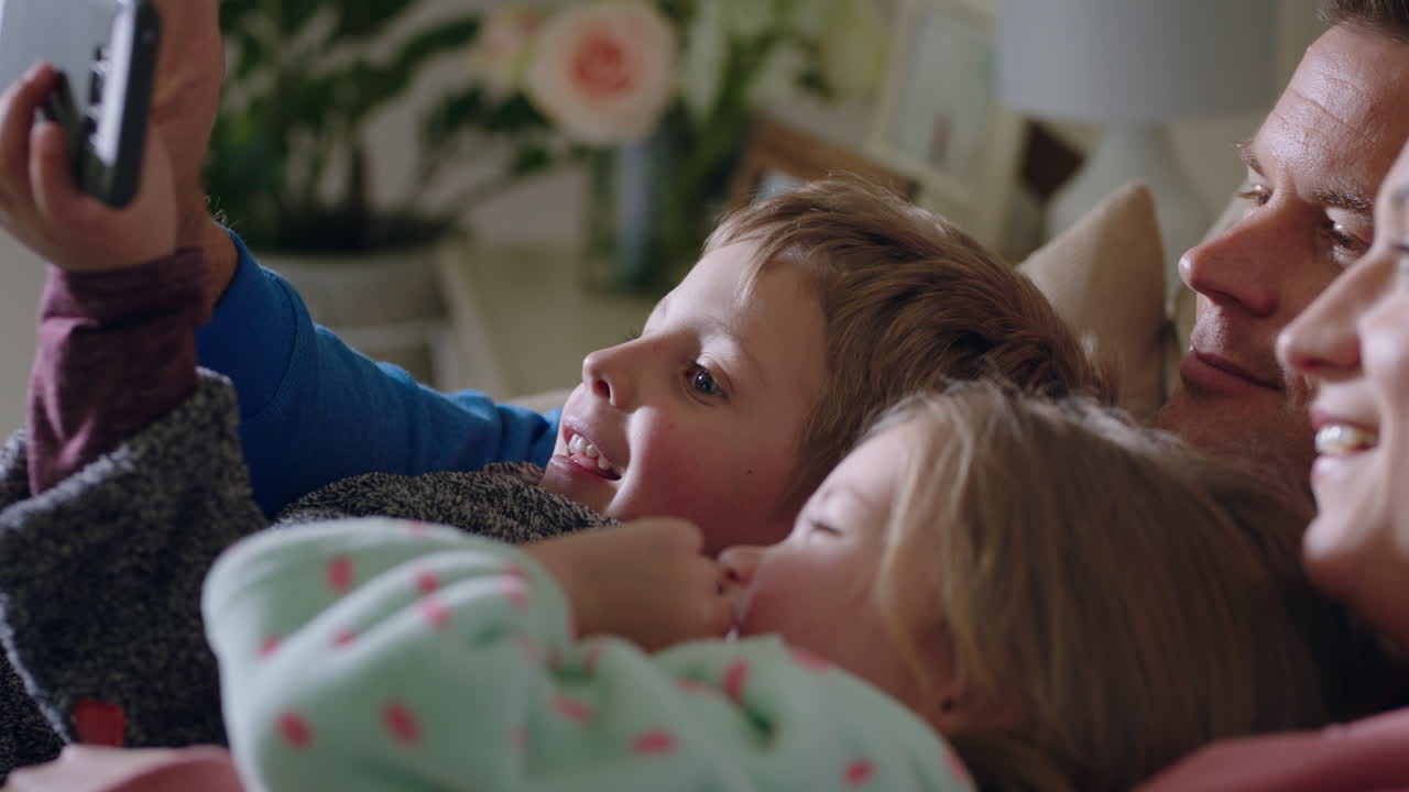 famiglia felice con bambini video chat utilizzando smartphone agitando lo schermo godendo della comunicazione del telefono cellulare a casa