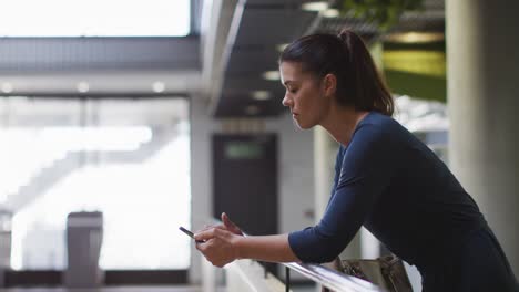 smiling caucasian businesswoman using smartphone in corridor in modern office