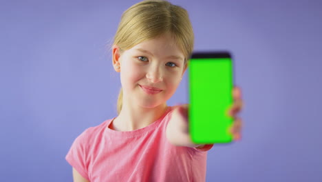 studio portrait of girl using mobile phone with green screen against purple background