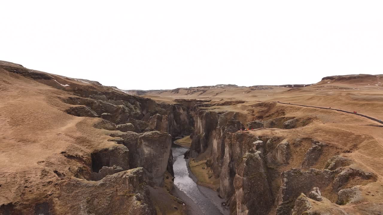 Drone ascends and unveils the full grandeur of Fjaðrárgljúfur Canyon, with steep rock walls and winding river below, near Kirkjubæjarklaustur, Iceland.