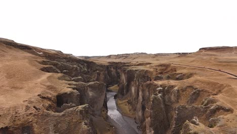 drone ascends and unveils the full grandeur of fjaðrárgljúfur canyon, with steep rock walls and winding river below, near kirkjubæjarklaustur, iceland.