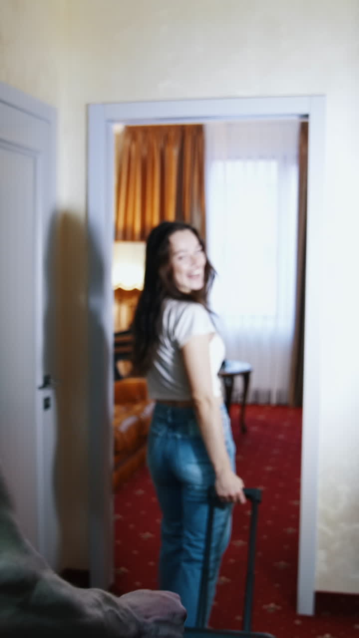 Young couple returning home. Travelers man and woman with suitcases coming into the room in the hotel during summer vacation. Vertical video