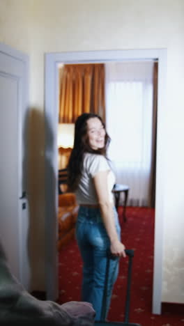young couple returning home. travelers man and woman with suitcases coming into the room in the hotel during summer vacation. vertical video