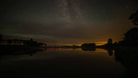 Tiro-De-Lapso-De-Tiempo-De-Estrellas-Visibles-Justo-Antes-Del-Amanecer-Sobre-Un-Camino-Al-Lado-De-Un-Lago-En-El-Campo-Rural