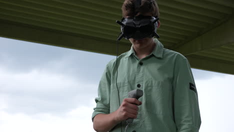 young man standing with goggles headset on head, holding remote motion controller