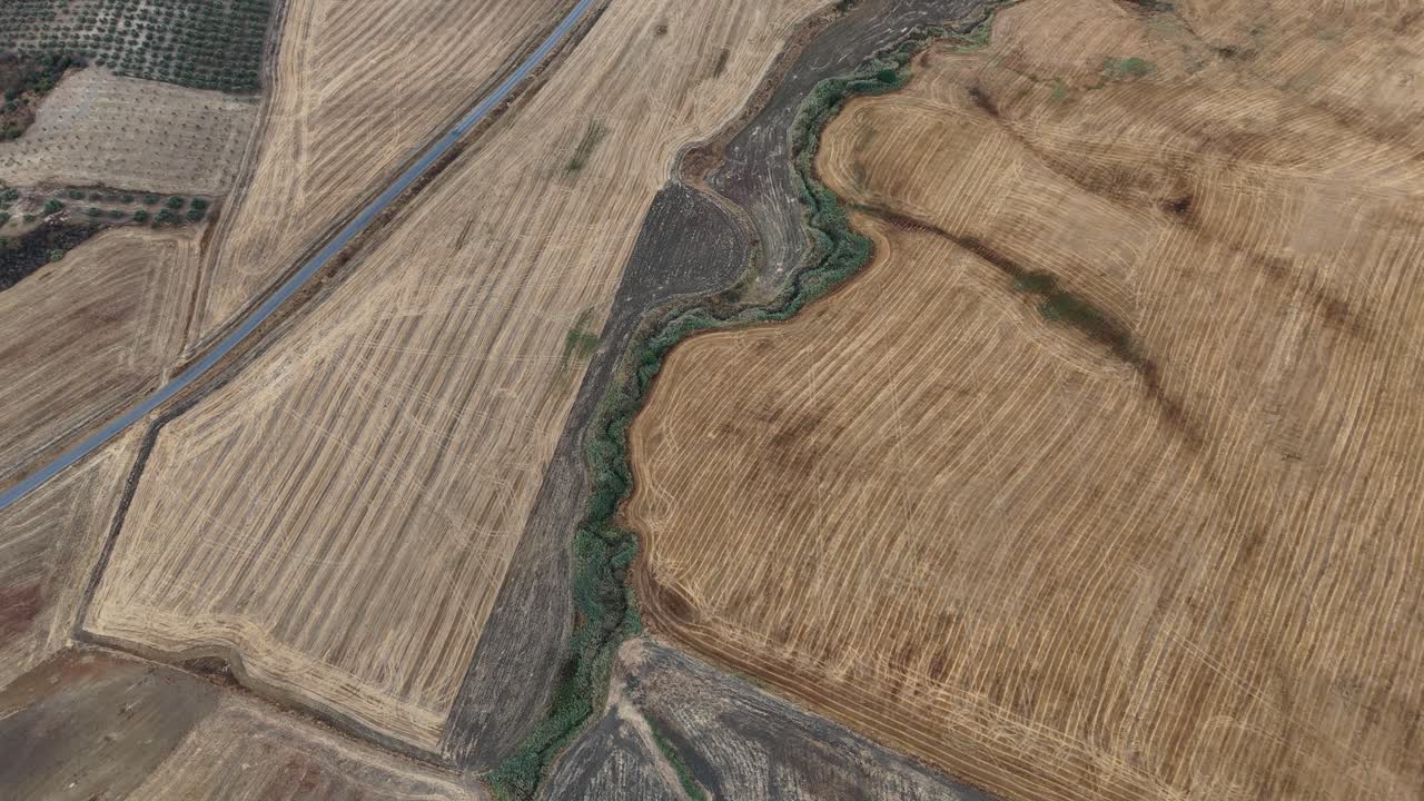 Top-down drone view of the farmland around Turón Castle in Ardales, Málaga, Spain, showing roads, a strip of green, dry fields, and scattered trees