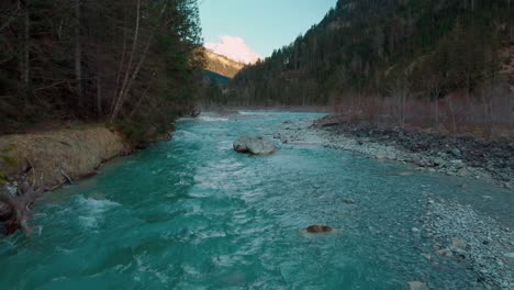 low aerial drone flight along a scenic mountain river with fresh blue water in the bavarian austrian alps in sunshine, flowing down a riverbed along trees, forests, rocks and peaks