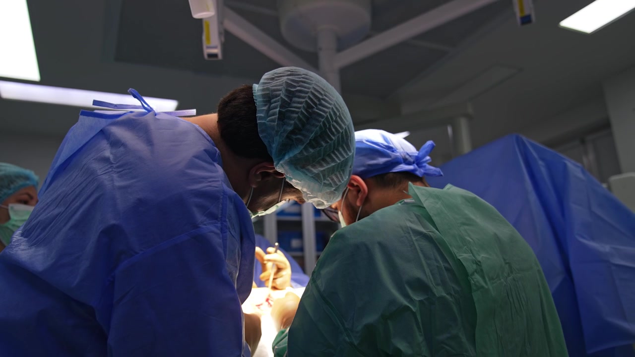 Vista posteriore di due chirurghi caucasici che eseguono un'operazione su un arto infortunato. Professionisti medici al lavoro utilizzano strumenti durante un intervento chirurgico per trauma.
