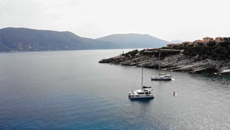 Boats-Floating-In-The-Calm-Ocean-With-5-star-Hotel-On-The-Hill-Near-Paralia-Emplisi-In-Greece