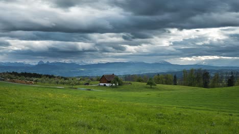 Dicke-Graue-Wolken-Ziehen-über-Den-Himmel,-Malerisches-Bauernhaus-Auf-Einem-Hügel-Auf-Einer-Wiese