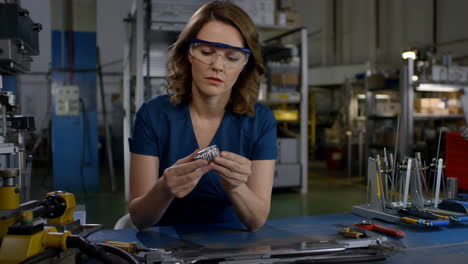 woman inspecting a metal part in a manufacturing facility