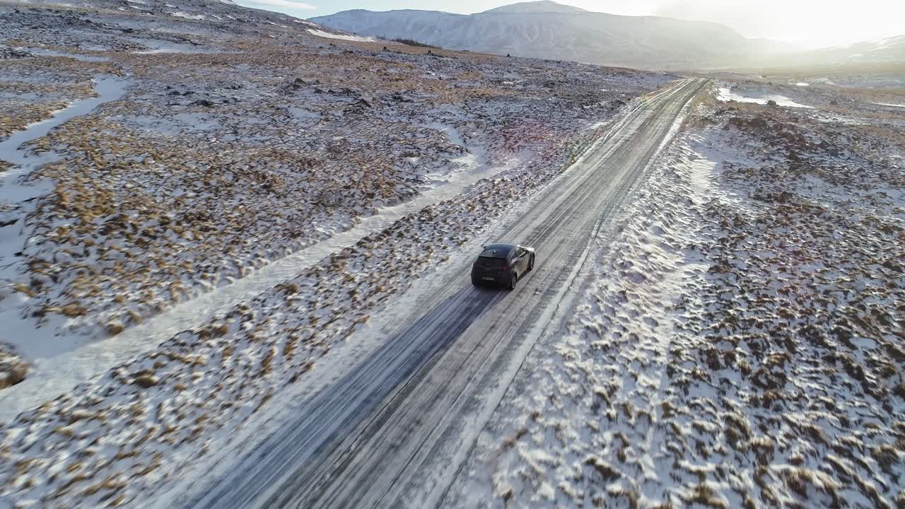 un coche negro conduciendo con cuidado por la carretera resbaladiza rodeada de campos nevados en islandia en una mañana soleada - toma aérea
