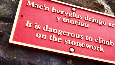 red metal warning climbing stone wall sign english welsh multilingual signage dolly left