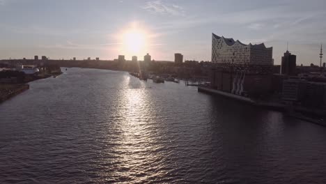 pan alrededor vista aérea del río ondulado y la ciudad moderna de hamburgo con el elbphilharmonie en primer plano contra el cielo nublado al atardecer