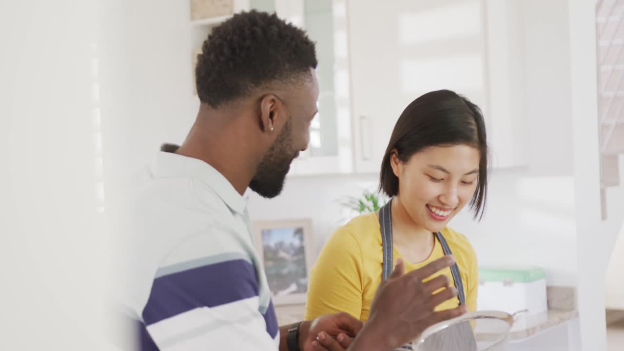 Happy diverse couple wearing apron and baking in kitchen