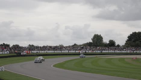 track-side view of old cars racing side by side into turn one at the goodwood revival car festival