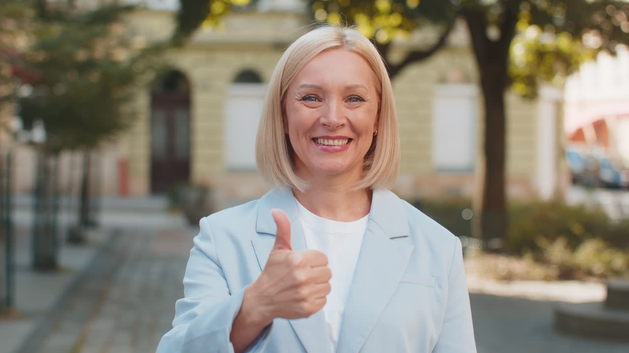 Smiling mature caucasian blonde businesswoman in formal suit looking camera and showing thumb up