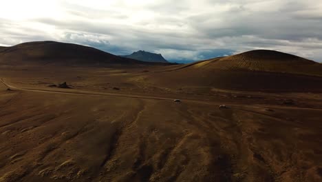 Vista-Aérea-Del-Paisaje-Sobre-Los-Vehículos-Con-Tracción-En-Las-Cuatro-Ruedas-Que-Viajan-Por-Un-Camino-De-Tierra-En-Las-Tierras-Altas-De-Islandia