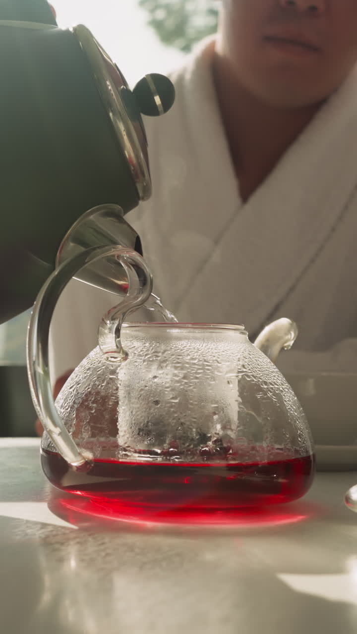 мужчина постепенно наполняет чайник для приготовления фруктового чая. молодой человек использует чайник с чайником и натуральную чайную смесь для подготовки здорового напитка в утреннее время