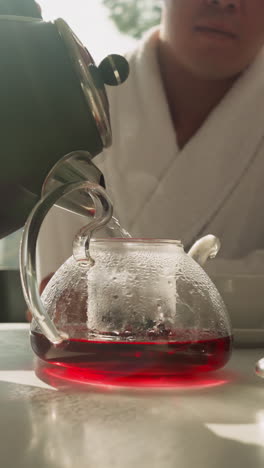 el hombre llena gradualmente la tetera para preparar té de frutas. el joven usa la tetera de la tetera y la mezcla de té natural para preparar una bebida saludable por la mañana
