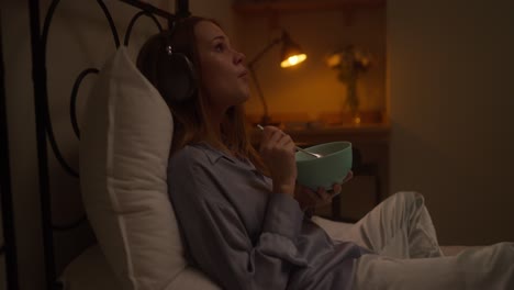 woman eating breakfast in bed with headphones