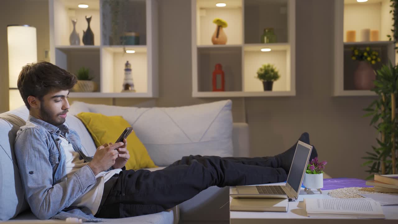 Man lying on the sofa at night texting on the phone. Happy and in good spirits.