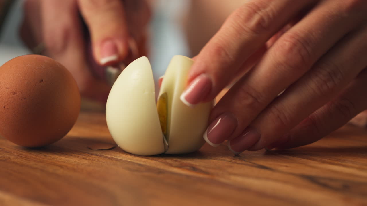 Slicing Peeled Hard-boiled Egg Into Halves On A Wooden Board. close-up shot