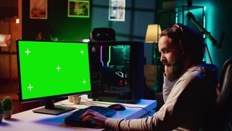 Green-screen-laptop-next-to-man-having-fun-by-using-gaming-keyboard-to-fly-spaceship-in-SF-videogame