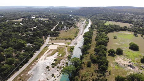 Rising-above-large-expanse-of-river-with-open-recreational-areas,-homes,-fields-and-trees-in-foreground