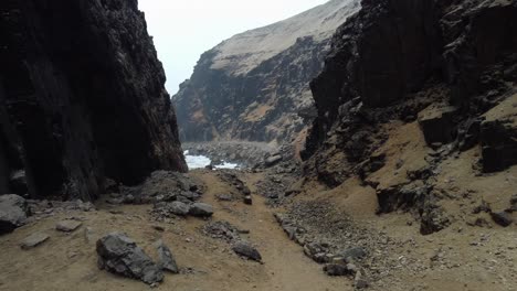 drone video of a person walking through gorge or mountain pass by a rocky beach