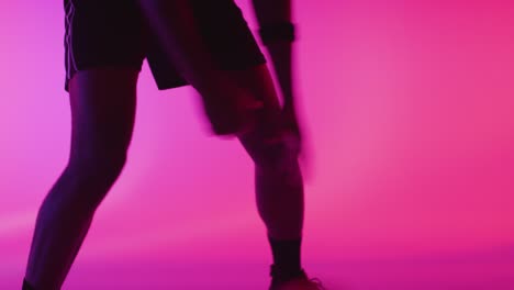 close up studio portrait of male basketball player dribbling and bouncing ball against pink lit background 5