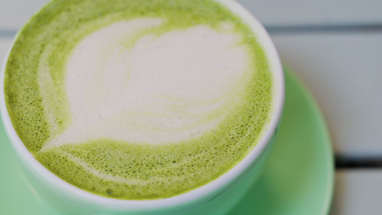 Close up of a matcha latte in a green cup on a terrace table