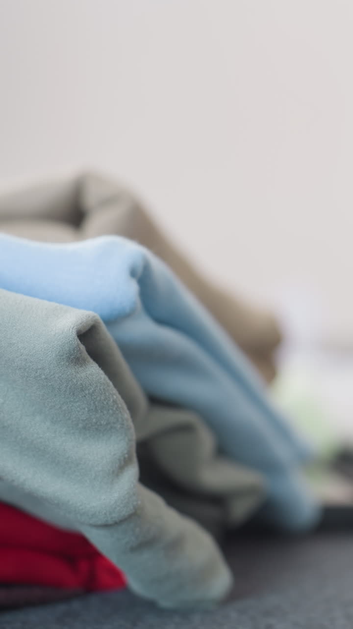 밝고 미니멀한 침실 환경의 표면에 개어 놓은 양털 의류, 파스텔 블루, 회색 및 빨간색 톤의 클로즈업 텍스처 연구, 아늑한 따뜻함, 세탁 관리, 옷장 정리, 소매를 연상시킵니다.