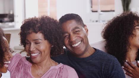 Happy-middle-aged-parents-sitting-at-home-with-their-teen-and-young-adult-kids,-panning-close-up