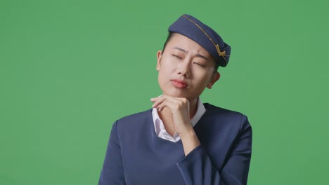 녹색 스크린 배경 스튜디오에 서 있는 동안 무언가에 대해 생각하고 주변을 둘러보는 아시아 여성 에어 호스테이스의 클로즈업