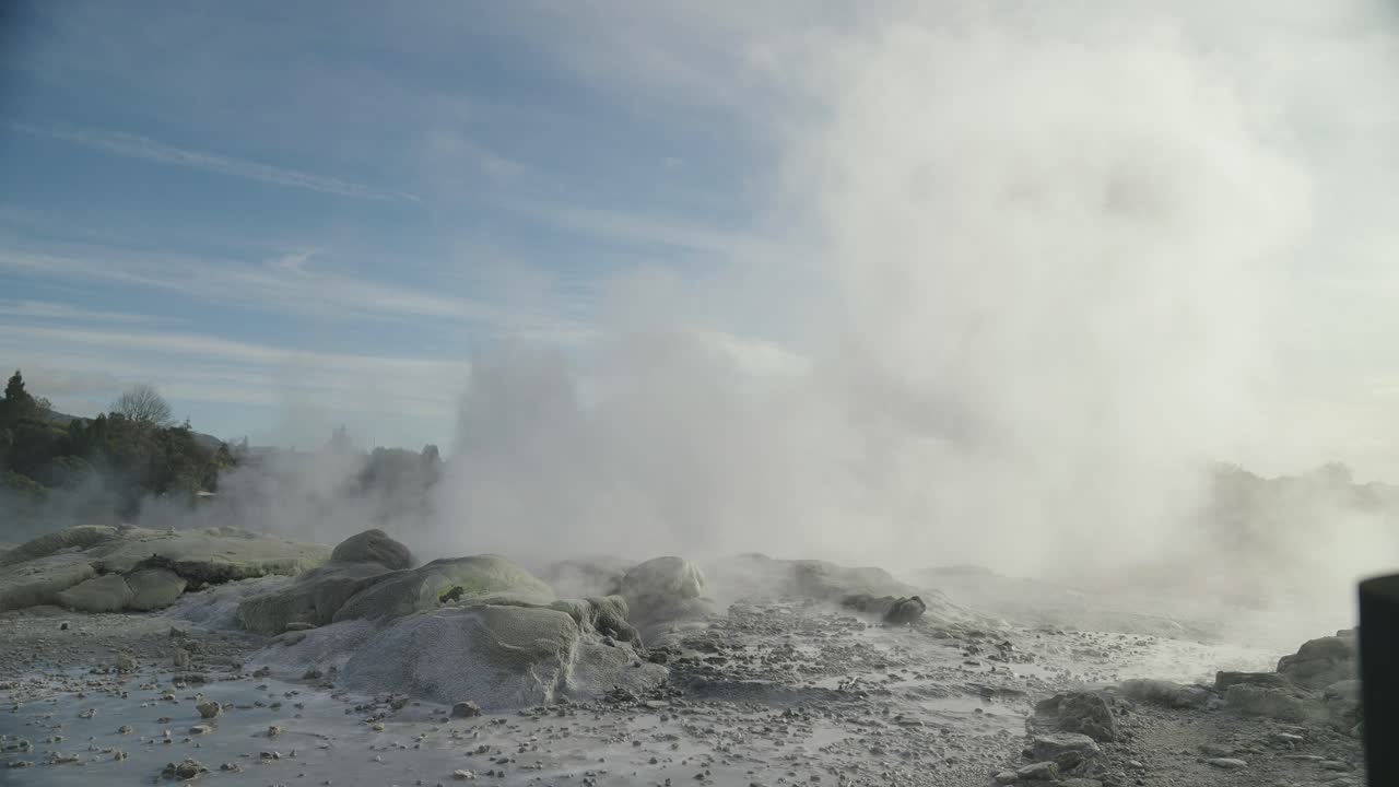géiser geotérmico en erupción con vapor y agua rodeado de naturaleza, rotorua, nueva zelanda, cámara lenta icónico ambiente rocoso de vapor, cielo soleado durante el día