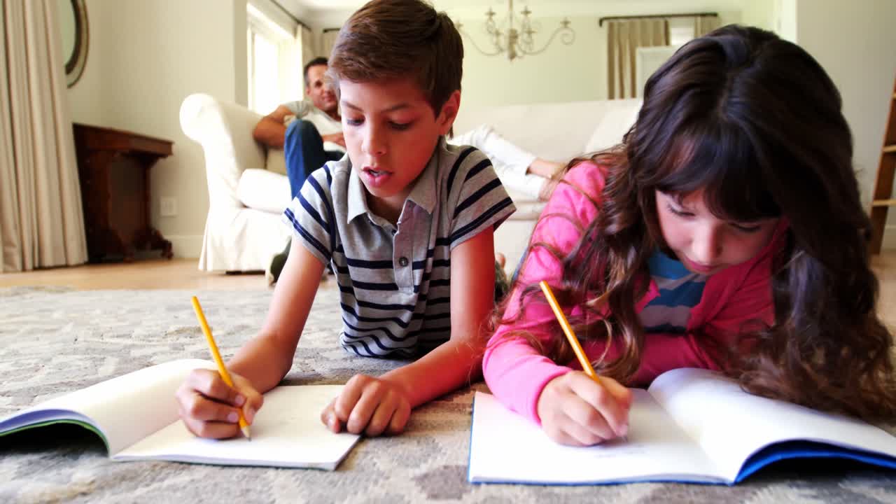 hermanos haciendo la tarea mientras se acuestan en la alfombra en la sala de estar