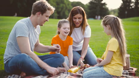 Padres-Felices-Con-Dos-Hijas-Pequeñas-Haciendo-Un-Picnic-Juntos-En-Un-Prado-Verde-En-El-Parque