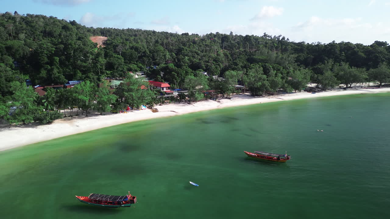 Boat anchored near shore of tropical island with green hills in Koh Rong, Cambodia, aerial pullback